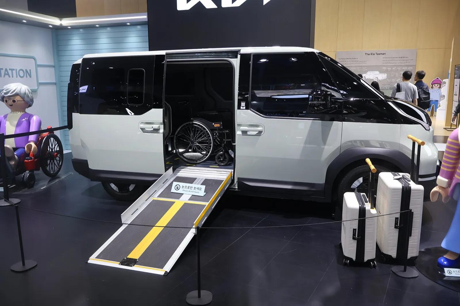 Kia PV5 WAV blanca expuesta en el Salón de la Movilidad de Seúl con la puerta lateral abierta, la rampa desplegada y una silla de ruedas en el interior