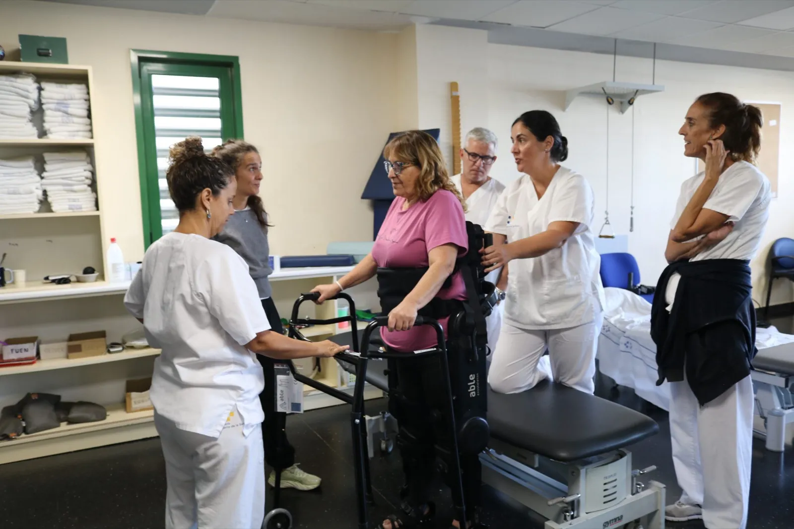 Una paciente camina con el exoesqueleto robótico y un andador en la sala de rehabilitación del Hospital Doctor José Molina Orosa, rodeada de fisioterapeutas
