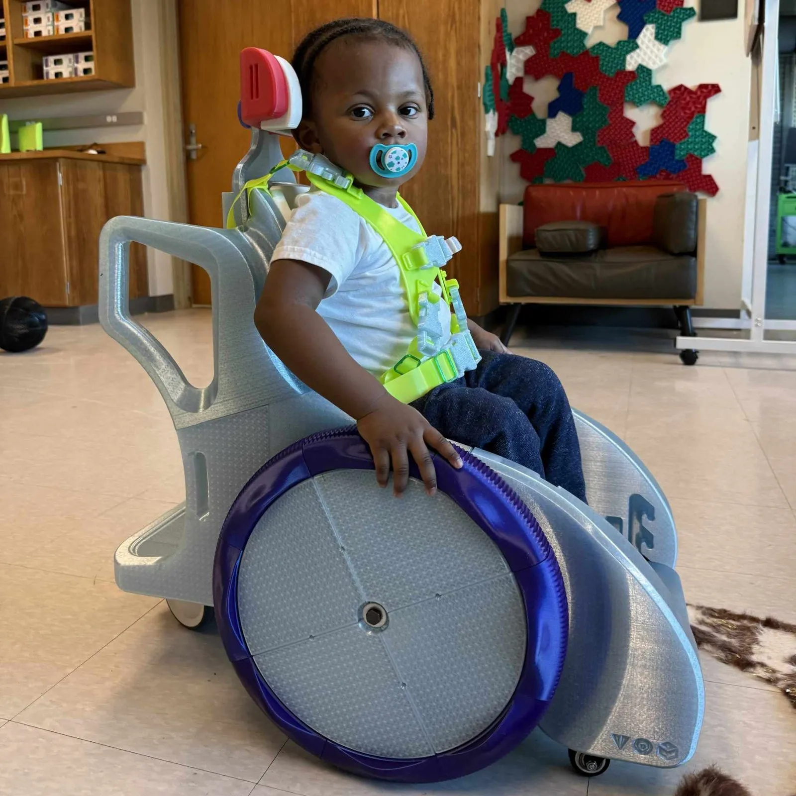 Un niño pequeño sentado en el vehículo de movilidad infantil de MakeGood, impreso en 3D, con ruedas grandes de color azul
