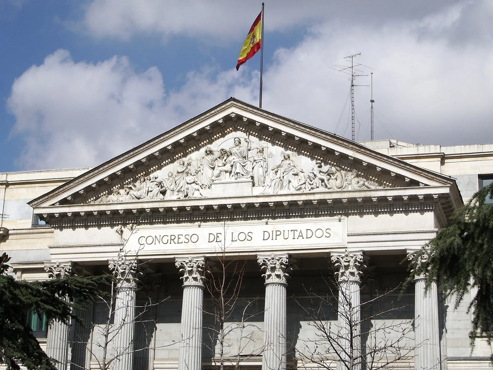 Frontón y columnas de la fachada principal del Congreso de los Diputados, en Madrid, con la bandera de España, un día de nubes