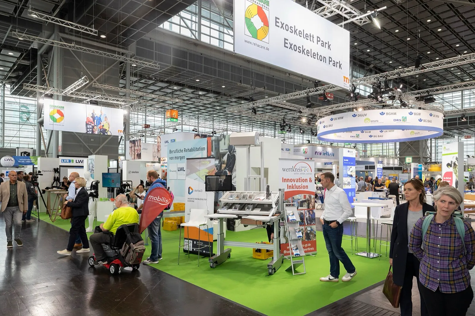 Visitantes, algunos en silla de ruedas eléctrica, recorren un estand de la feria REHACARE en Messe Düsseldorf (edición de 2022)