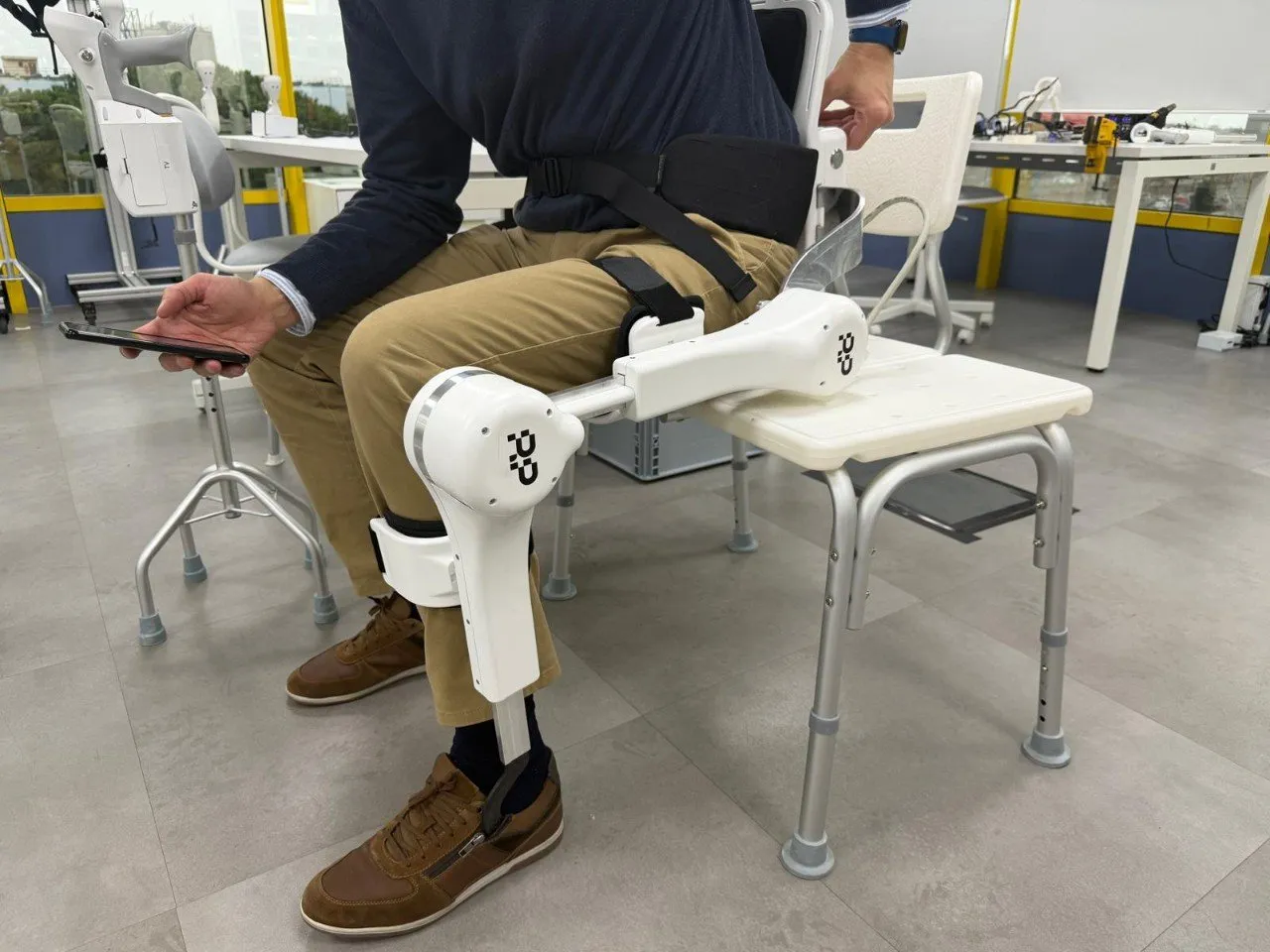 Un hombre sentado prueba el dispositivo Awake de Robopedics, una pierna robótica blanca sujeta al muslo y a la pierna