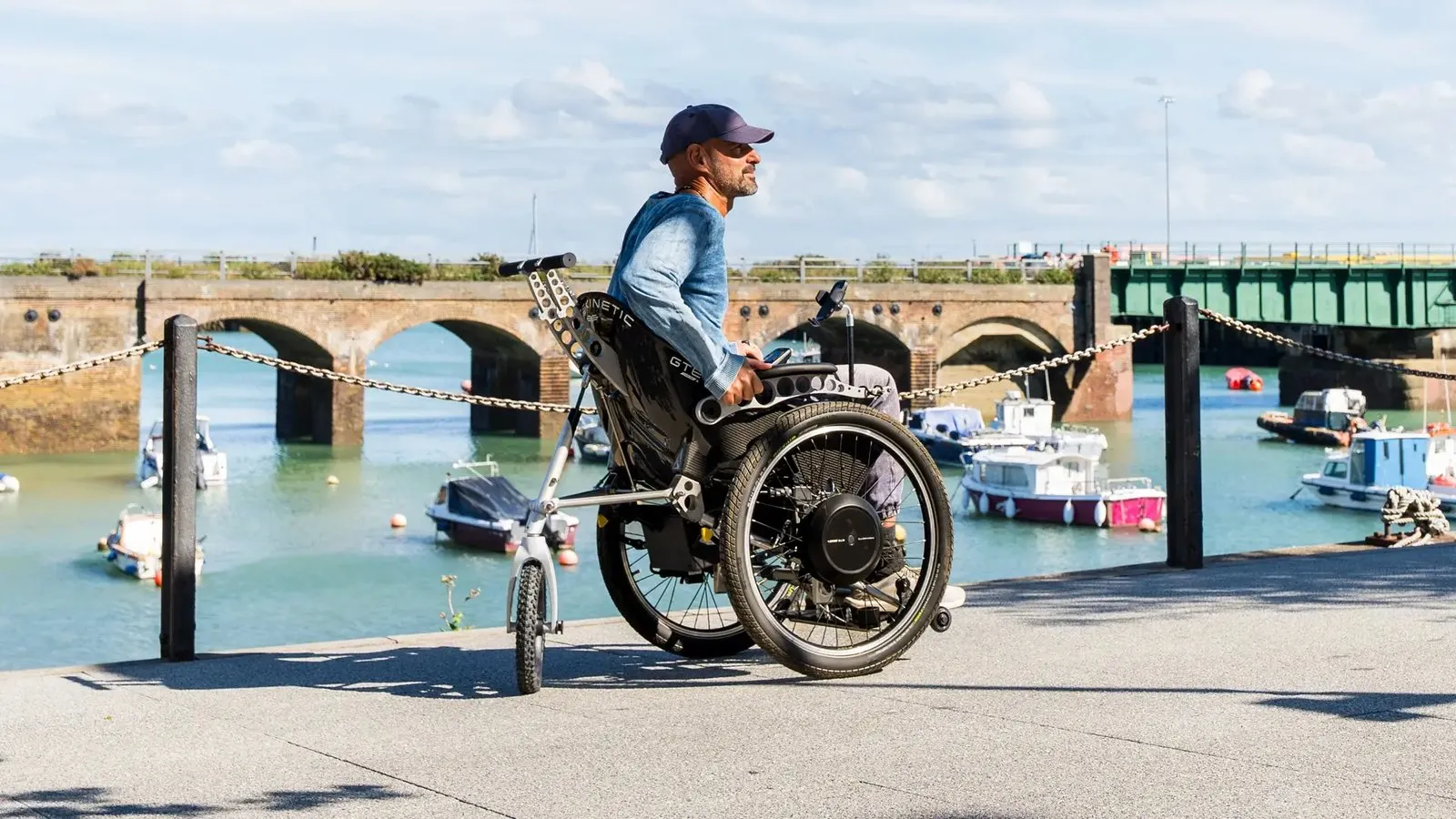 Un hombre recorre un muelle junto a un puerto en la silla eléctrica todoterreno Trekinetic GTE Series 4