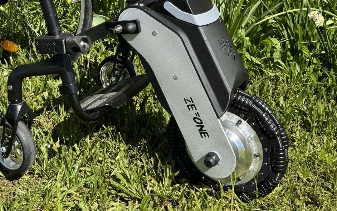 El módulo eléctrico Ze One de WheelMove acoplado a la parte delantera de una silla de ruedas manual, sobre la hierba