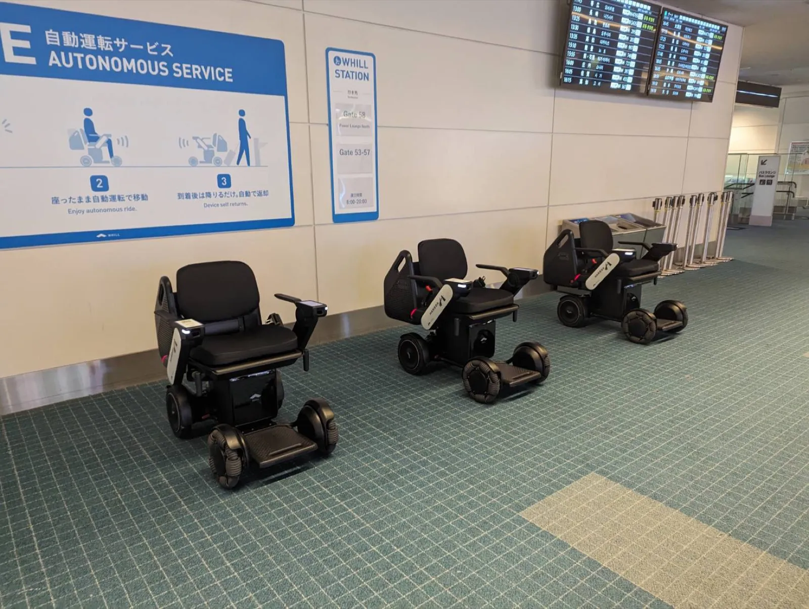 Tres sillas de ruedas autónomas WHILL aparcadas junto a una estación de servicio autónomo en una terminal del aeropuerto de Haneda (Tokio)
